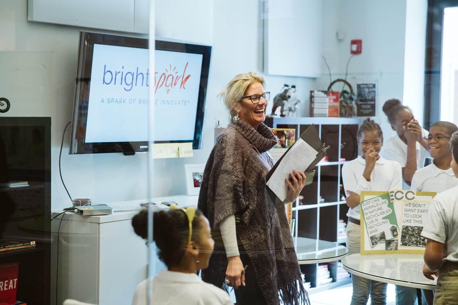 A presenter with students at a Bright Spark session, the Bright Spark logo on the screen